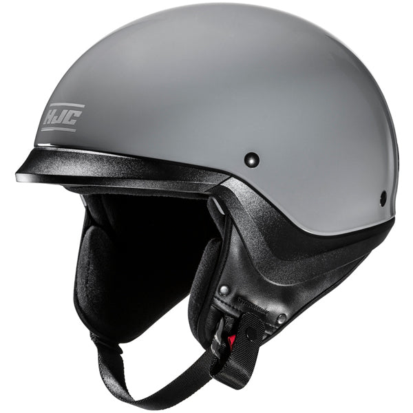 822020503 | A sleek, modern motorcycle helmet with a smooth, matte gray finish, featuring a black padded interior and chin strap with a red buckle, set against a plain white background. The helmet has a rounded shape with minimalistic design, small black ventilation holes on the sides, and a subtle logo on the front left side. The lighting highlights the helmet's contours and matte texture, creating soft shadows that emphasize its aerodynamic form. | Available at BTO Sports - alternate view