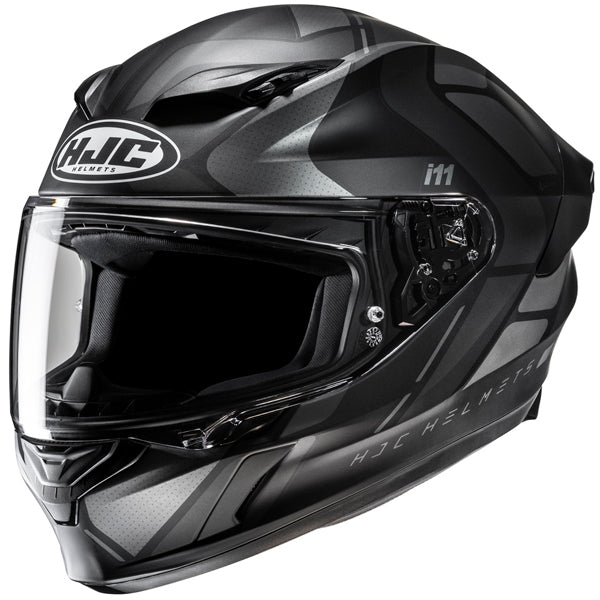 810410103 | A sleek, modern motorcycle helmet in matte black and gray with angular design elements, featuring a clear visor, ventilation vents on top, and the HJC logo prominently displayed on the front. The helmet has a streamlined shape with subtle branding and model markings, set against a plain white background with soft lighting that highlights its contours and reflective surfaces. | Available at BTO Sports