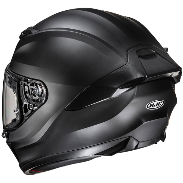 A sleek, matte black motorcycle helmet with a smooth, aerodynamic design, featuring a clear visor with internal mechanisms visible, and a small, oval HJC logo on the side. The helmet has subtle curves and vents, with a slightly glossy finish that reflects light, set against a plain white background. The image is taken from a slightly angled side view, highlighting the helmet's contours and detailed features, with soft, even lighting that emphasizes its modern, professional style.