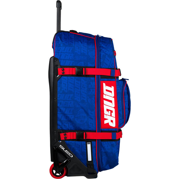 Side profile view of the blue OGIO RIG 9800 DNGR X bag with large white DNGR vertical logo, red straps, telescoping handle, and exposed SLED base and wheel frame. SKU 80100024 | Available at BTO Sports