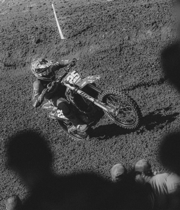 Motocross rider on a dirt bike in action on a track with spectators watching. 100% Goggles collection