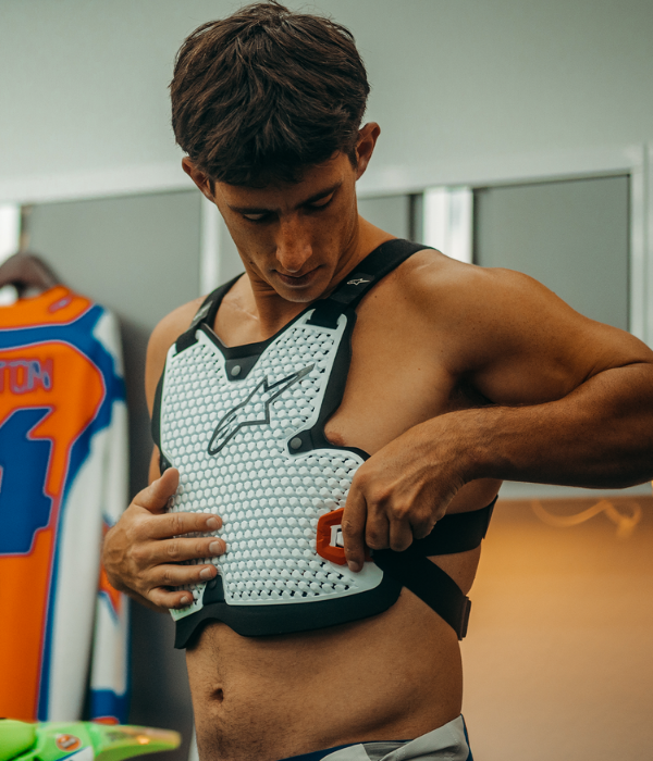 Rider adjusting an Alpinestars motocross chest protector before riding, highlighting lightweight impact protection and adjustable straps. collection