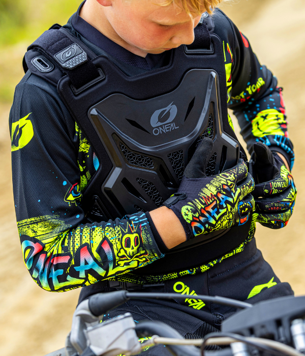 Young rider wearing an O'Neal youth motocross chest protector and colorful riding gloves while adjusting protective gear before riding. collection