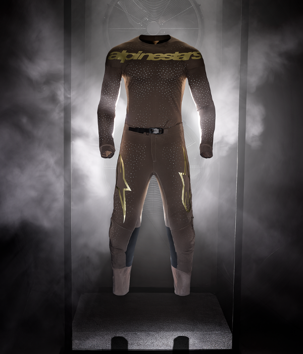 Alpinestars Supertech motocross jersey and pants displayed in a dramatic smoke-filled studio with illuminated backlighting. collection