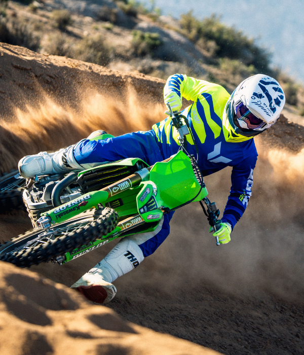 Motocross rider in bright blue and neon yellow Thor gear carving a green dirt bike through a sandy berm and throwing up dirt. collection