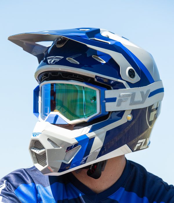 Close-up of a FLY Racing motocross helmet with matching blue goggles worn by a rider on a sunny day. collection