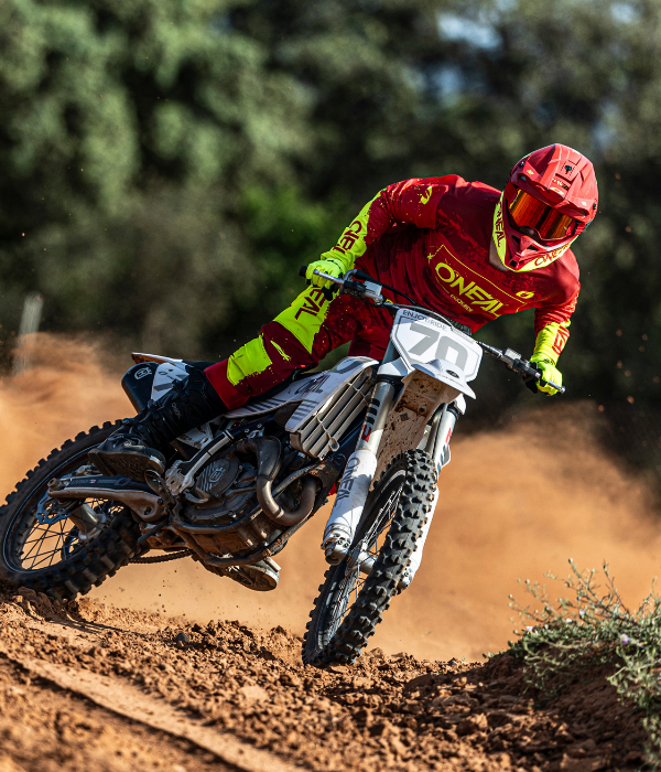 Rider carving through a berm wearing O'Neal red and neon yellow motocross gear on a dirt bike during an off-road race. collection