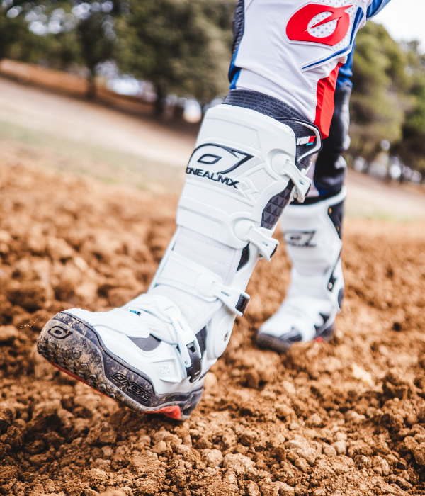 Close-up of white O'Neal motocross boots walking across a dirt track, highlighting premium protection and buckle design. collection