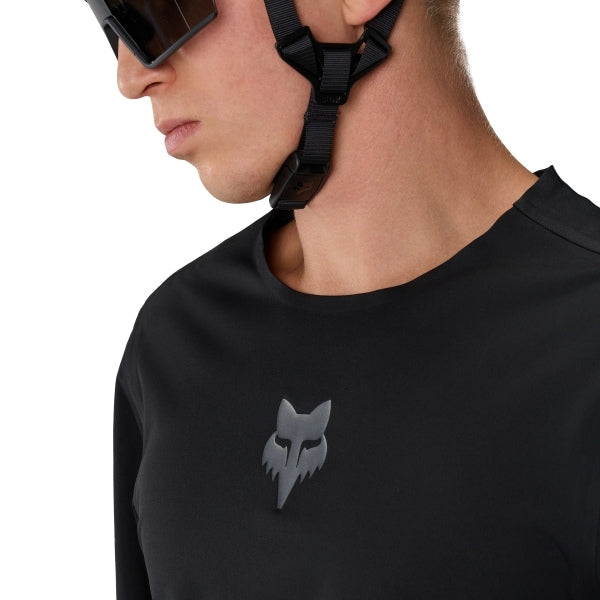 Fox Racing Flexair Water Pullover (MTB) in Black, modeled chest and shoulder view, with the close-fitting black body, long sleeves, small Fox chest logo, and curved hem worn by a mountain bike rider. Available options—Color: Black; Size: SM, MD, LG, XL, 2X. SKU 40141-001-L. UPC 198571107997.