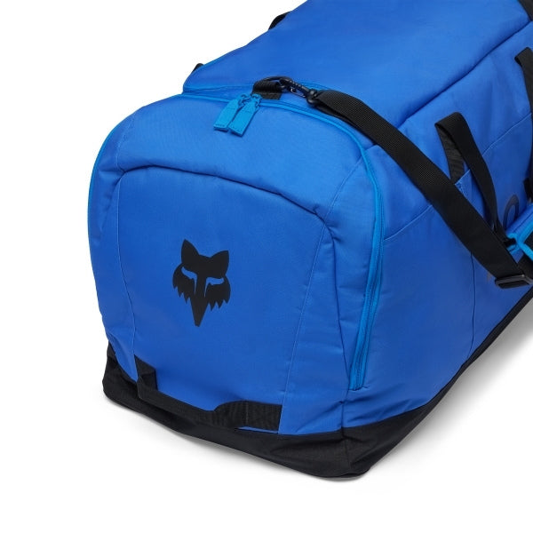Fox Racing Podium Duffle in Blue Jewel, opposite long-side view, with the main zippered compartment, reinforced base, carry handles, end pocket, wheels, and large Fox logo. Available options—Color: Black, Red, Blue Jewel. - alternate view