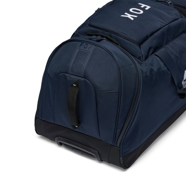 Fox Racing Shuttle Roller Bag in Midnight, opposite long-side view, with the main zippered compartment, reinforced base, carry handles, end pocket, wheels, and large Fox logo. Available options—Color: Black, Pewter, Midnight.