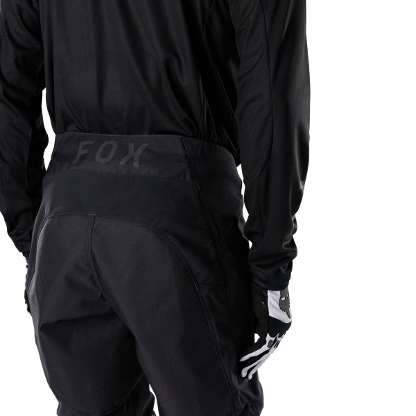Fox Racing 180 Blackout Pants in Black, close-up of the ratcheting waist closure, with the ratcheting waist adjuster, stretch yoke, shaped hip panel, and reinforced knee or thigh material. Available options—Color: Black; Size: 26, 28, 30, 32, 34, 36, 38, 40, 42, 44. SKU 40693-001-32. UPC 198571121955.