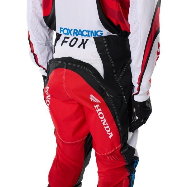 Fox Racing 180 Honda Pants in White/Red, close-up of the ratcheting waist closure, with the ratcheting waist adjuster, stretch yoke, shaped hip panel, and reinforced knee or thigh material. Available options—Color: White/Red; Size: 26, 28, 30, 32, 34, 36, 38. SKU 40708-077-32. UPC 198571132807.