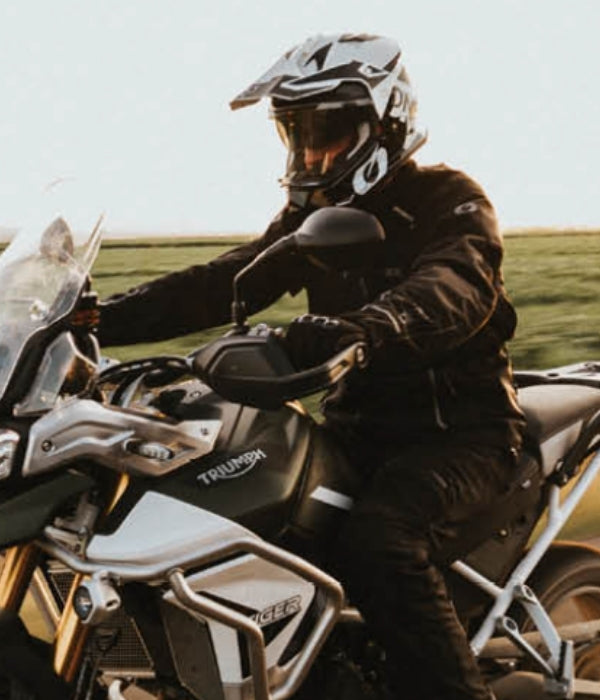 Person on a Triumph motorcycle with a helmet and leather jacket in a scenic setting Oneal collection