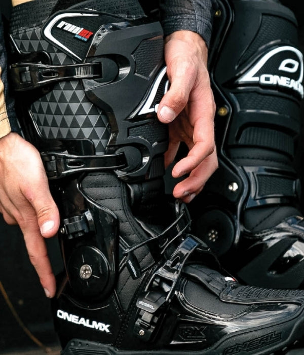 Close-up of black motorcycle boots with 'Oneal' branding, held by a person. O'Neal collection