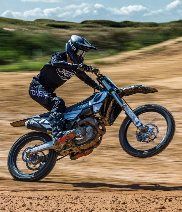 Person riding a dirt bike on a dirt track with a blurred background O'Neal MX26 Riding Gear collection