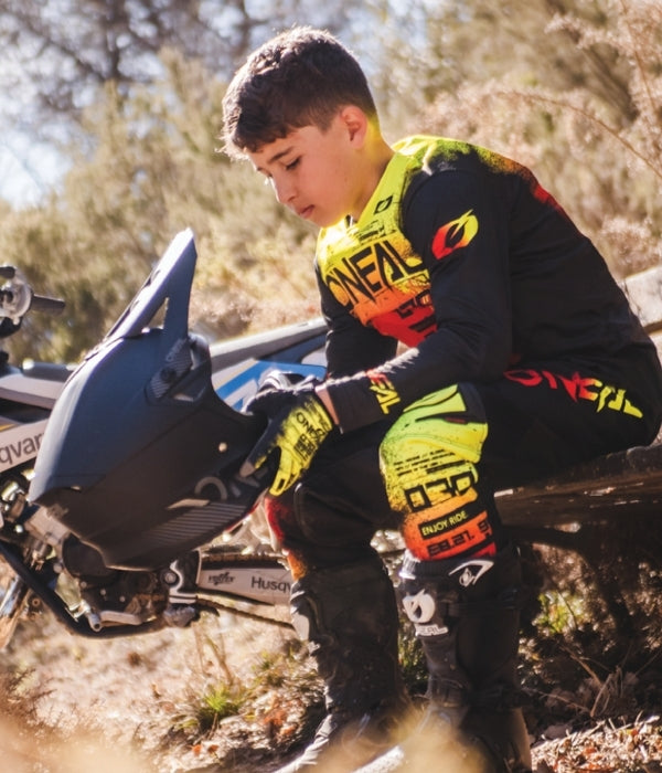 Person in motocross gear kneeling next to a motorcycle in an outdoor setting Oneal Youth collection