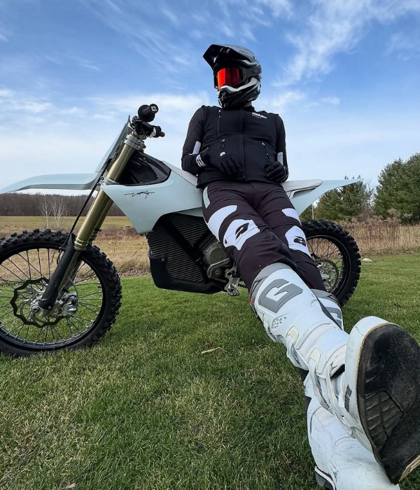 Motocross rider in black gear sitting on an electric dirt bike in an open grassy field under blue sky collection