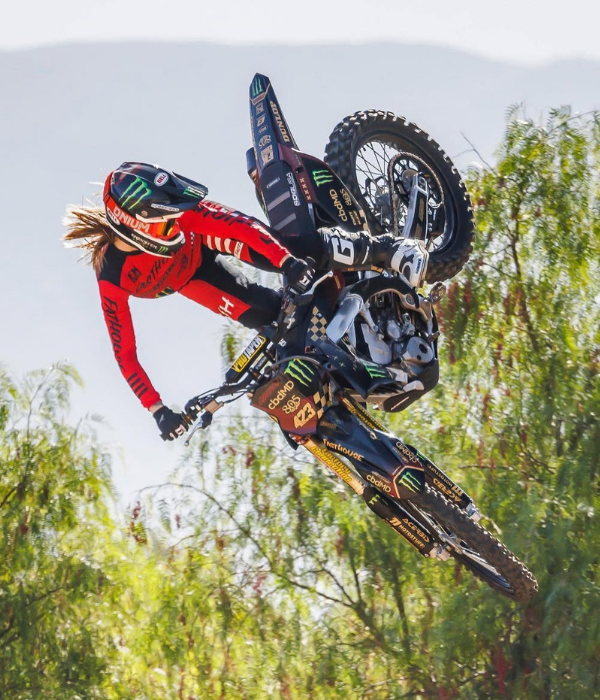 Motocross rider in red gear performing a whip trick mid-air on a dirt bike with trees in the background collection