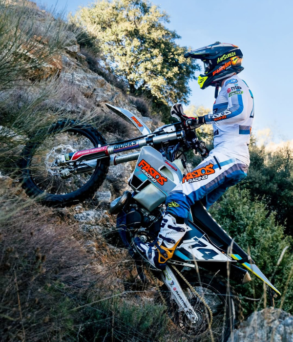 Motocross rider in white and blue gear climbing a rocky hillside trail on a dirt bike collection