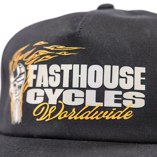 Fasthouse Spanner Hat SKU 3210050 in black, angled front view with flat brim, displaying Fasthouse Cycles Worldwide logo and flame piston artwork, motocross streetwear snapback.