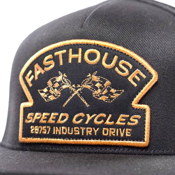 Close-up front view of the gold embroidered patch on the Fasthouse Crown hat (SKU: 3210150). The patch, featuring checkered flags and the