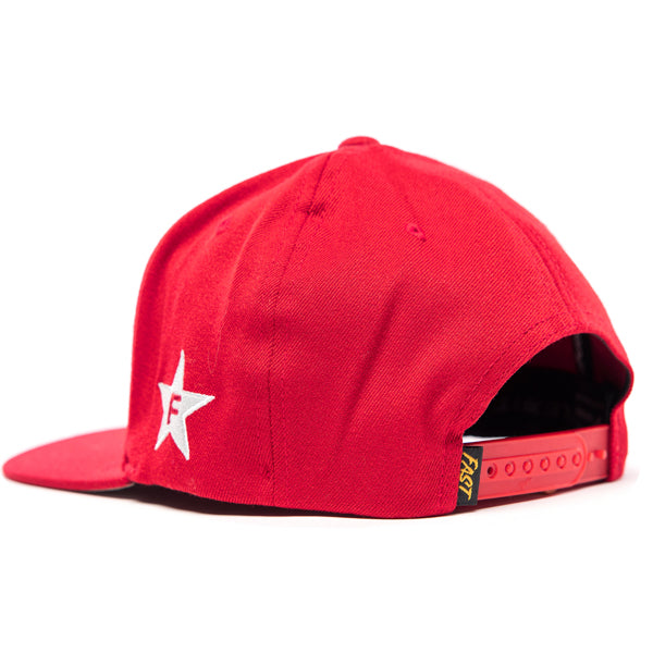 A back view of the red Fasthouse Crown Hat (SKU 3210150), showing the adjustable snapback closure. The plastic snapback is red, matching the hat's main color. A small, yellow tag with the