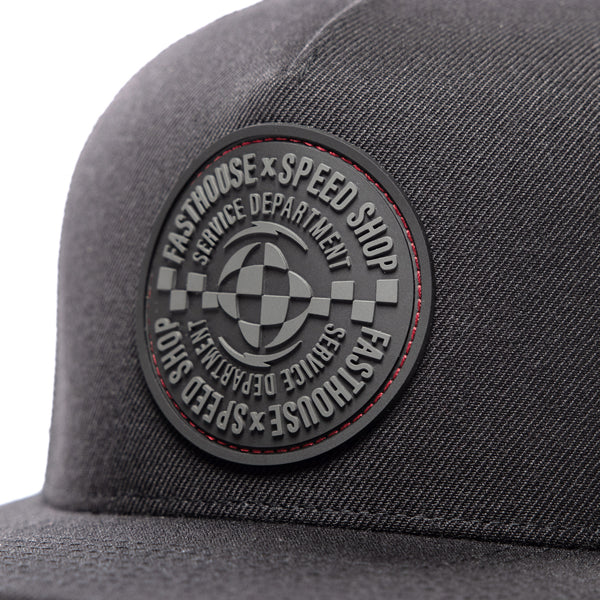 Close-up of Fasthouse Finch Hat SKU 3210070 – detailed view of the embossed Fasthouse Speed Shop circular rubber patch with checkered flag design and fine stitching on the black front panel.