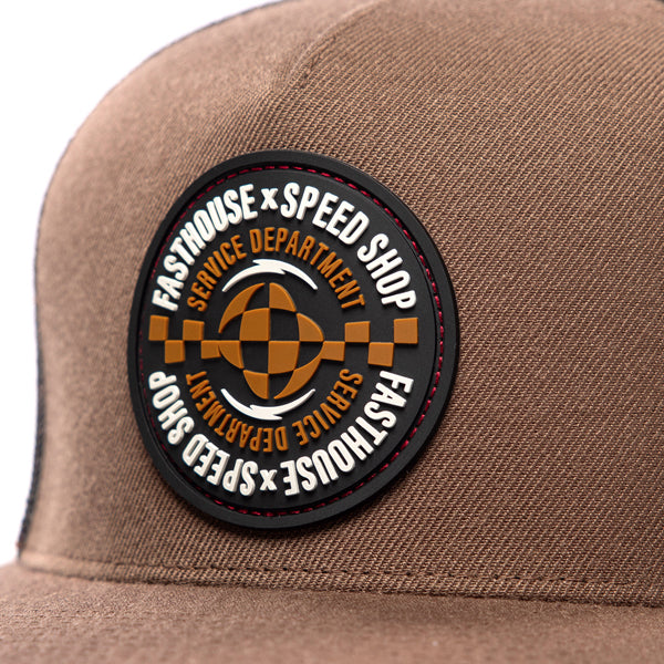 Close-up of Fasthouse Finch Hat SKU 3210070 showing detailed round Speed Shop Service Department patch with orange checkered racing design, durable stitching, motocross-inspired snapback style.