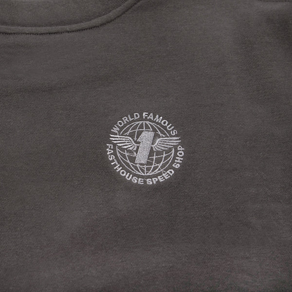 Close-up of Fasthouse Renown Crew Neck Crop Women’s Pullover in black, SKU 32139005. Detail of embroidered chest logo with winged number one inside globe and text reading “World Famous Fasthouse Speed Shop,” styled for motocross and racing culture.