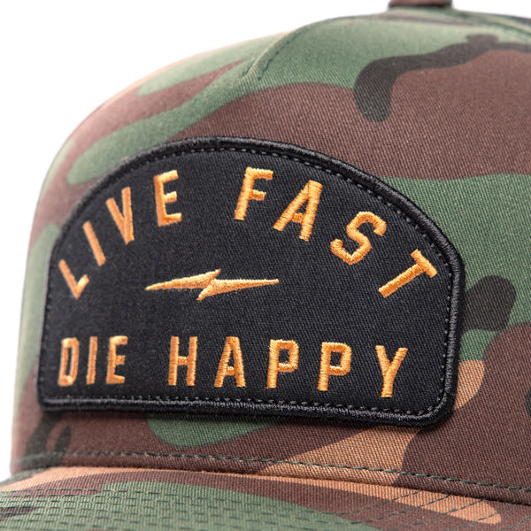 Close-up view of Fasthouse Wired Hat SKU 3321098 camo design showing the black patch with gold embroidered text “Live Fast Die Happy” and a lightning bolt in the center, emphasizing motocross lifestyle branding.