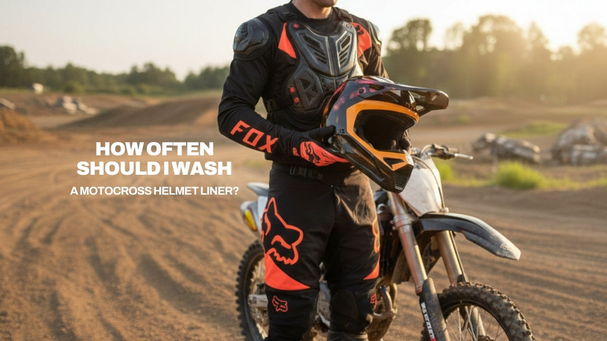 A rider in Fox gear holding a helmet at a dirt track, featuring the text: How often should I wash a motocross helmet liner?