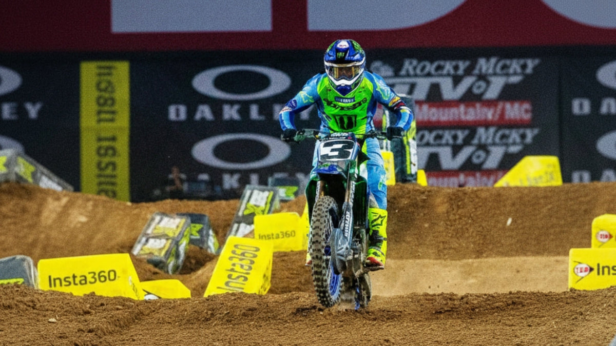 A professional motocross racer wearing blue and lime green gear with the number 3 on their bike, navigating a dirt track jump. This features prominent branding from Oakley and Insta360 in the background of a stadium racing environment.