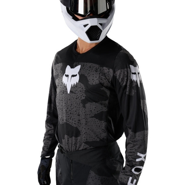 Fox Racing 180 BNKR Jersey in Black Camo, modeled front three-quarter view, with the crew neck, long sleeves, contrasting shoulder and arm graphics, and extended rear hem on a rider. Available options—Color: Black Camo; Size: XS, SM, MD, LG, XL, 2X. SKU 40649-247-M. UPC 198571123324.