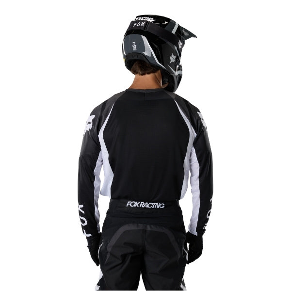 Fox Racing 180 Frame Jersey in Black, close-up of the lower hem and drop-tail panel, with the printed Fox artwork, mesh-knit texture, reinforced seam lines, and shaped cuff or hem. Available options—Color: Blue, Grey/Yellow, Black, Red; Size: XS, SM, MD, LG, XL, 2X, 3X. SKU 40665-001-2X. UPC 198571122242.