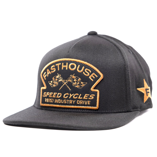 Front view of the black Fasthouse Crown hat (SKU: 3210150), a motocross snapback with a gold embroidered shield patch featuring crossed checkered flags and text that reads "Fasthouse Speed Cycles 28757 Industry Drive."
